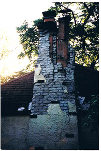 Chimney before repair. Bricks are crumbling and the top half of the flues are visible. Huge cracks down the remaining portion of chimney.